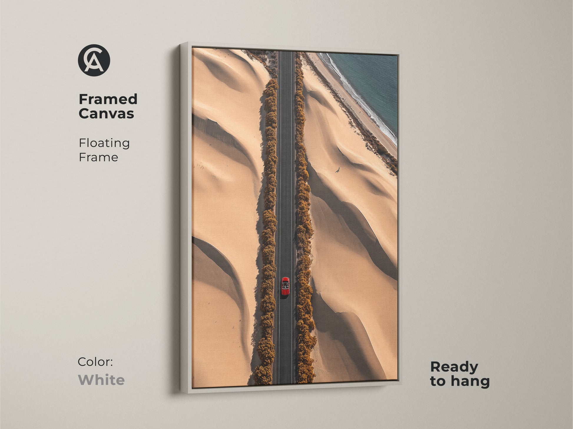 This desert road art print is framed in white. The aerial canvas features a red car on a sandy beige road. The contemporary travel art captures dunes and an ocean view. Ready to hang this artwork is a modern landscape for your home or office. It is a perfect gift for travel lovers.