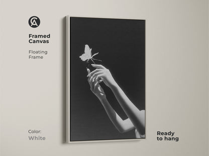A framed canvas presents monochrome butterfly art with hands reaching. Ready to hang with a sleek white floating frame it's minimalist. This surrealist wall decor makes a symbolic statement in modern homes. It’s an artistic wall hanging perfect as bedroom art. Enjoy this contemporary art.
