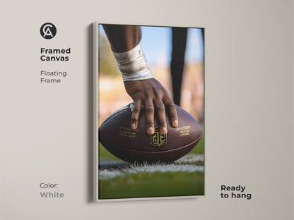 Framed Canvas Print of American Football Action. The artwork has a floating frame in white. The image is of a player's hand holding the football. Ready to hang instantly. This sports themed gift is great for any room. Perfect for football season wall art.