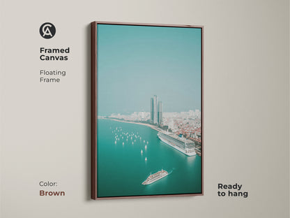 Framed canvas with a brown floating frame shows a teal ocean cityscape. It includes an aerial view of a cruise ship sailboats and city buildings. This contemporary travel artwork is perfect as a housewarming gift art.