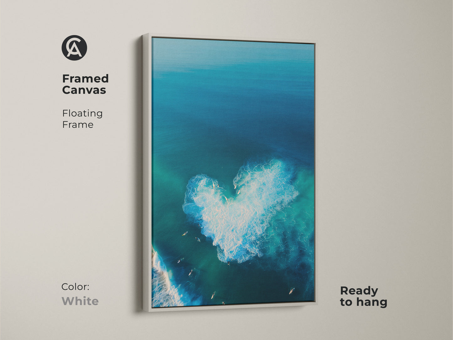 White framed canvas art showing a serene aerial ocean scene. A heart-shaped wave is visible. Surfers are enjoying the surf. This floating frame canvas is ready to hang. The white frame offers a clean modern look. The artwork brightens any space. 