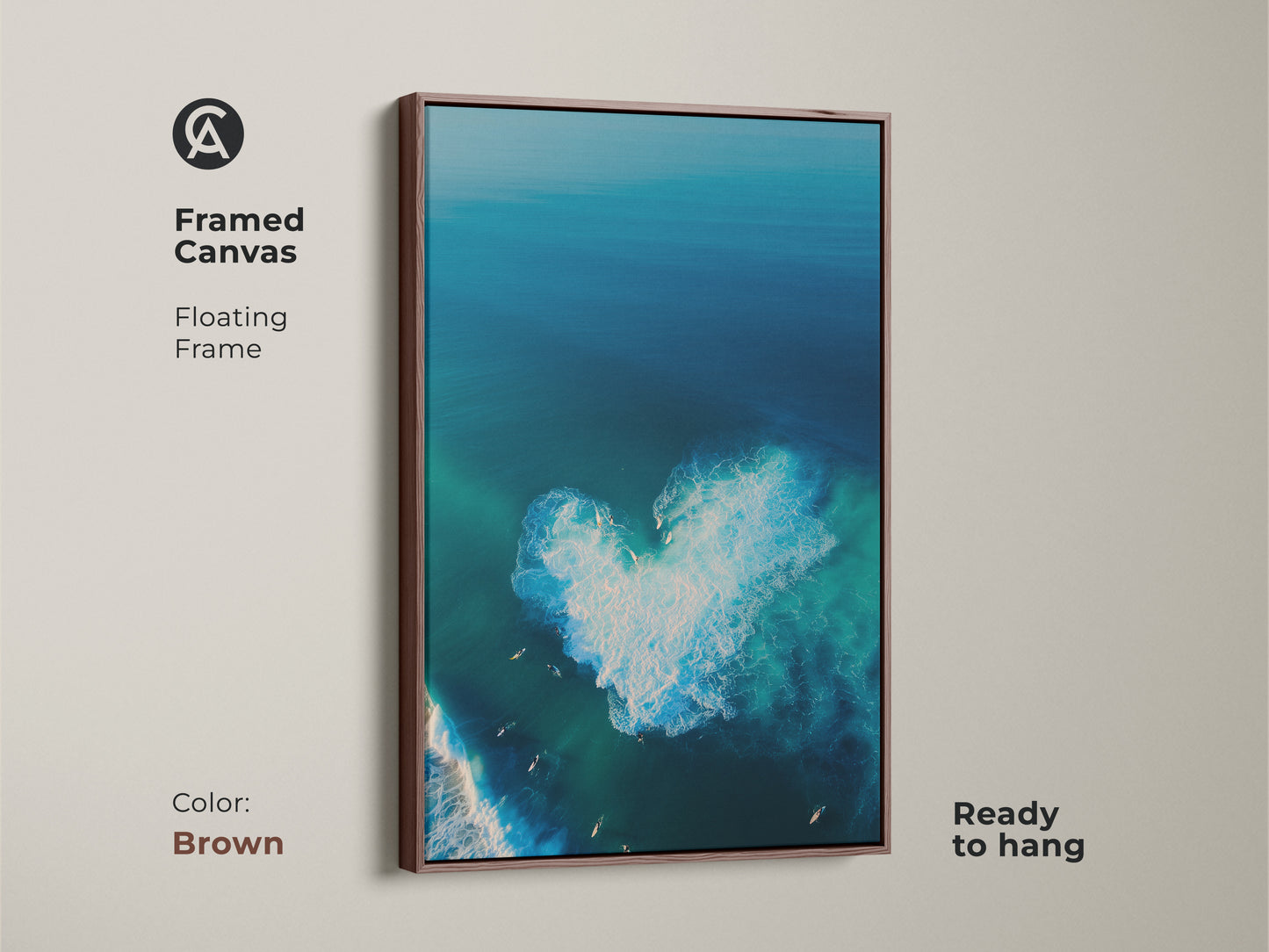 Brown framed canvas art displays a captivating ocean scene. From above you can see a heart-shaped wave. Several surfers dot the waters. This floating frame canvas is ready to hang. The warm brown frame complements the cool ocean tones. It's the perfect wall decor. 