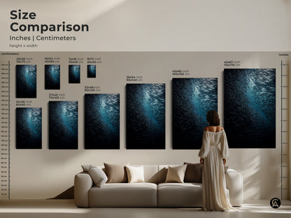 Size comparison of deep sea wildlife art in inches and centimeters. A woman views various sizes of the teal blue ocean canvas above a sofa. This school of fish artwork is perfect for coastal living room wall art. Find your ideal fit.