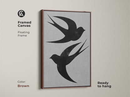Framed canvas art displays a black and white bird print. Two swallows are silhouetted against a textured gray backdrop. The floating frame has a brown finish and the art is ready to hang. A nature-inspired housewarming gift.