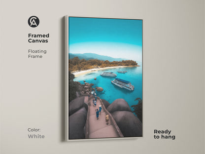 Framed canvas displaying an aerial island beach. White floating frame enhances the turquoise ocean view art. This coastal landscape wall art is ready to hang. The boat filled bay print captures a tropical island getaway. It's a blue water seascape with a summer vacation vibe. Ideal for beach house decor.