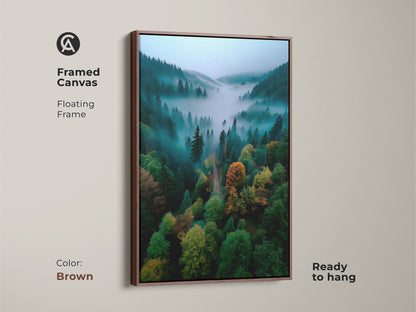 Framed canvas artwork showcasing a misty forest landscape. The brown floating frame complements the natural scene. Ready to hang this piece adds warmth to any space. The lush trees and foggy valley create a calming atmosphere.