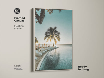 White framed coastal canvas art print. The serene tropical paradise shows a palm tree and infinity pool. This artwork brings relaxed summer vibes to your home. A perfect addition to your tropical living room art.