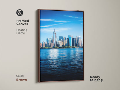 Framed canvas featuring the New York City skyline. This photorealistic New York art print has a floating frame in brown. Ready to hang this blue cityscape is waterscape NYC skyline art. Perfect as a New York lover gift print.
