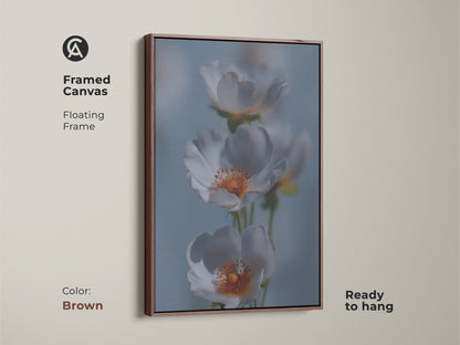 Framed canvas featuring delicate white flower artwork. This soft focus botanical art is in a brown floating frame. The light blue floral canvas is perfect for bedroom wall art. A gentle flower art print adds a serene feel. It's a beautiful housewarming gift for Scandinavian style homes.