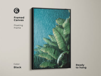 Black framed canvas print of tropical banana leaves in the rain. The green botanical wall art is ready to hang. The floating frame enhances the moody green teal artwork. This botanical art is a perfect boho plant lover gift. Ideal for bedroom decor or a calming office plant wall.
