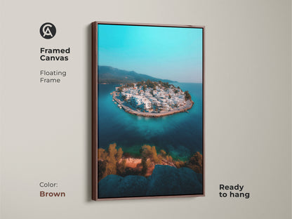 A framed canvas in brown showcases a captivating aerial view of a turquoise coastal village. The floating frame complements the deep blue seascape and white buildings. Ready to hang this artwork adds an elegant travel-inspired touch. It's a perfect piece for modern coastal home decor enhancing a travel theme.