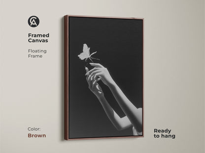 Framed canvas displaying monochrome butterfly art. This surreal hands print is ready to hang. Its floating frame enhances this piece of minimalist art. Ideal as bedroom art the brown frame is the perfect gift for dreamers. This piece is a fusion of contemporary elegance and symbolic nature art.