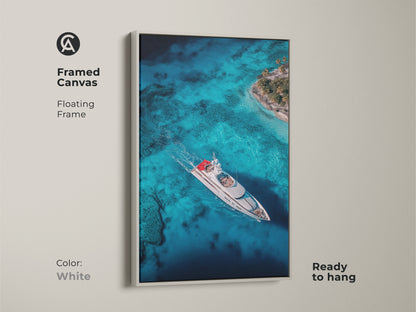 White framed canvas artwork featuring a yacht sailing on pristine turquoise waters near a tropical island. The floating frame gives a clean modern look. This ready-to-hang piece adds a fresh coastal vibe to any room. Ideal for those seeking minimalist elegant nautical-themed wall decor.