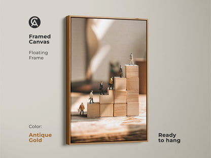 Framed canvas featuring miniature people climbing wooden blocks is enhanced with an antique gold floating frame. This motivational office artwork adds a touch of elegance to any workspace. The beige tan minimalist canvas print serves as a constant reminder of success and career growth. Ready to hang it is a perfect gift for business owners.