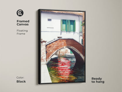 Framed canvas art features a Venetian canal with a brick bridge and red water reflections. The black floating frame enhances the traditional European cityscape. Ready to hang for a classic wall decor touch.