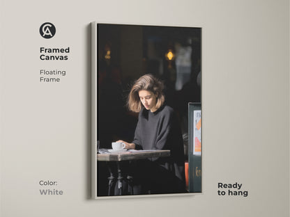 White framed canvas print. Features a woman reading at a cafe. A minimalist black and white art piece. A stylish addition to any modern home or office space.