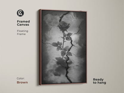 Brown framed canvas showing gothic rose artwork. The floating frame highlights dark floral artwork with a rose from cracked earth. This surreal botanical art is in black white and gray tones. Ready to hang this piece enhances gothic decor. This is symbolic rose art for eclectic home decor.