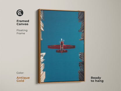 Framed canvas featuring a red aeroplane soaring in a deep blue sky over urban skyscrapers. The floating frame is antique gold. This aviation art print brings a contemporary feel. This is ready to hang and perfect as an aviation enthusiast gift.
