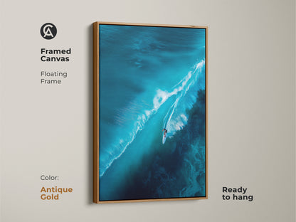 Framed canvas artwork of a surfer riding a large turquoise wave. The floating frame is antique gold. The ready-to-hang wall art is elegant. Enhance your space with this sophisticated ocean-inspired art.