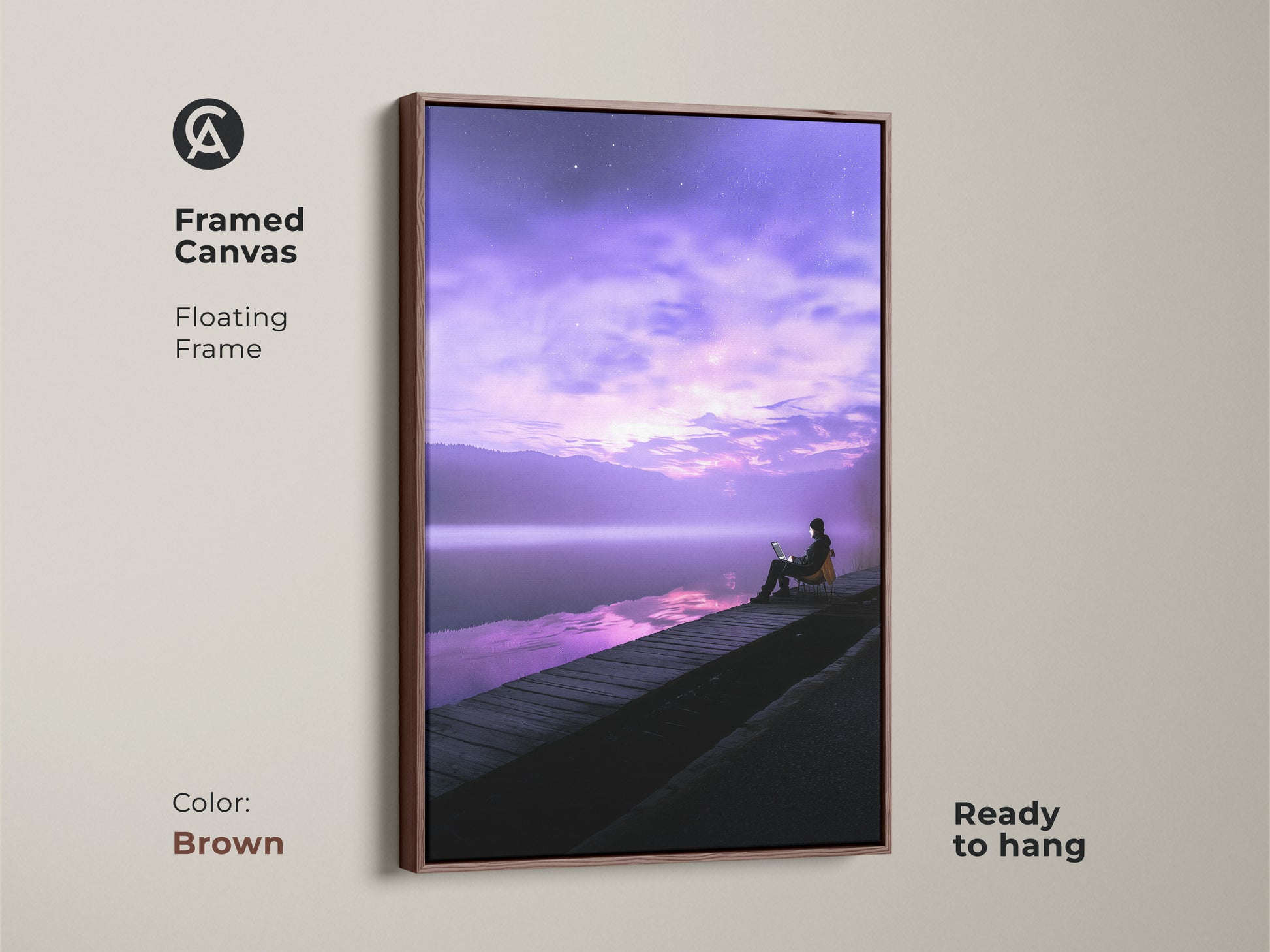 Framed canvas art showing a person working on a laptop by a tranquil lake. The floating frame is in brown. This modern landscape artwork features a violet skyscape. Ready to hang. Perfect wall decor for adding a calming touch to your workspace.