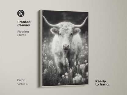 A white framed canvas print of a longhorn in a field. The black and white artwork is ready to hang. The floating frame offers a clean modern look. This fine art photograph is a versatile addition to your art collection.