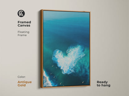 Antique gold framed canvas art features an ocean view. A heart-shaped wave is the focal point. Surfers ride the waves. This floating frame canvas is ready to hang. The antique gold frame adds a touch of elegance. It enhances the coastal artwork's appeal.