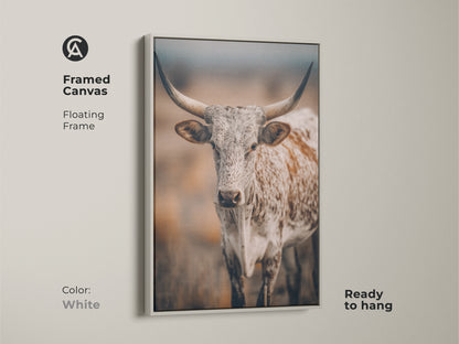 White framed canvas featuring Longhorn Cow artwork. This Texas wildlife canvas print has a floating frame. It is ready to hang. The neutral color palette complements any farmhouse decor. The artwork brings a touch of the country to your home.