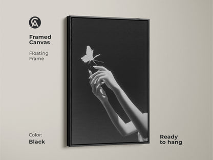Framed canvas featuring surreal hands reaching for a butterfly in monochrome. This minimalist black art is ready to hang. The floating frame adds a contemporary touch to the elegant insect artwork. This contemporary bedroom wall art is perfect for modern home decor. Its frame is in the color black.