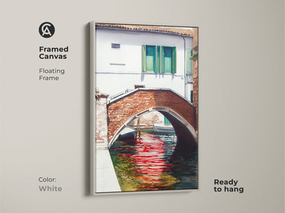 Framed canvas art displays a Venice canal scene with a brick bridge and red reflections. The white floating frame offers a clean look to the traditional artwork. Ready to hang and complements any decor.