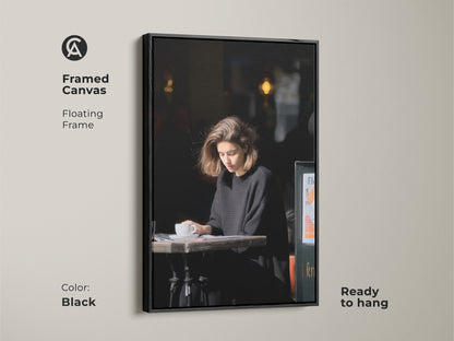 Framed canvas featuring a woman reading in a cafe. The black frame enhances the monochrome art. Ready to hang for a modern home office or living room. Elegant cafe artwork.