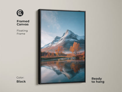 A framed canvas art print of a mountain landscape. This rustic nature wall decor is ready to hang. The floating frame enhances its scenic beauty. The artwork features snowy mountains and vibrant autumn colors reflected in a lake. The black frame complements its blue white and orange tones.