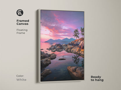 Framed canvas print featuring a coastal sunset with a white floating frame. The rocky coastline and pine trees are highlighted against a pink purple sky. This scenic nature print is ready to hang. Perfect for coastal or modern decor.