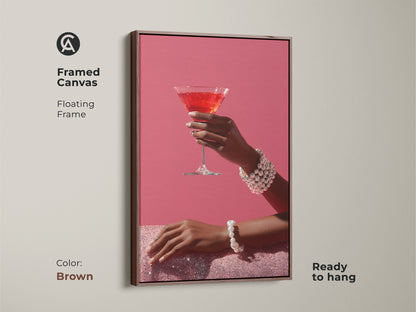 Add sophistication with this framed canvas of pink martini art. The brown floating frame enhances the artwork. It shows a hand with a pearl bracelet. This contemporary cocktail decor is ready to hang. Ideal glam bar wall art for a stylish touch.