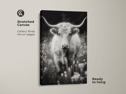 A stretched canvas print of a longhorn in a field. The black and white artwork is ready to hang. The gallery wrap canvas features mirrored edges. This fine art photography print adds a touch of rustic charm to any room.
