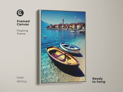 White framed canvas art capturing a European coastal town. The floating frame complements the blue boats on clear water. This realistic artwork is ready to hang adding a touch of nautical charm. Perfect as a housewarming gift for beach lovers.