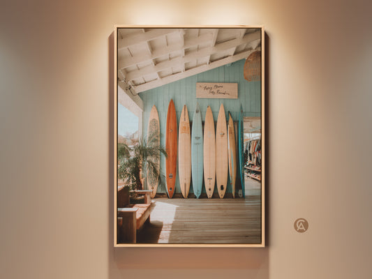 A collection of surfboards stands against a blue wall. Sunlight streams through a window onto the wooden floor. A potted palm adds a tropical touch. This vibrant photograph captures a surf shop atmosphere. Perfect coastal art for surf enthusiasts. Add a beach vibe to your home decor.