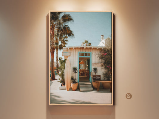 Framed canvas art featuring a tropical beach resort entrance. A surfboard leans against the building. Palm trees sway in the breeze. It brings a coastal vibe to your space. Perfect for beach lovers. The canvas art is ready to hang.