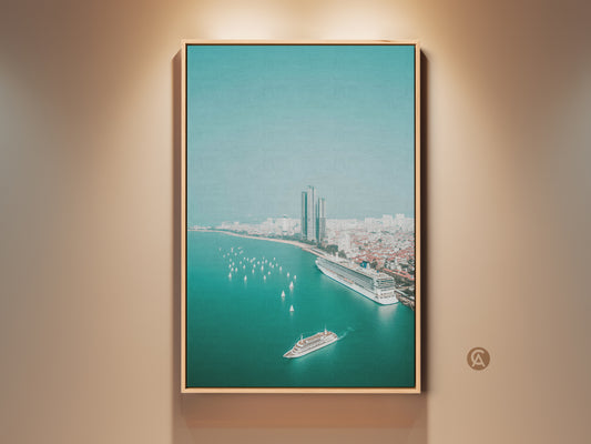 Teal ocean cityscape canvas print in a natural wood frame. An aerial view shows a cruise ship sailboats city buildings and the ocean. This coastal artwork is a contemporary travel gift idea and nautical themed art for living room decor.