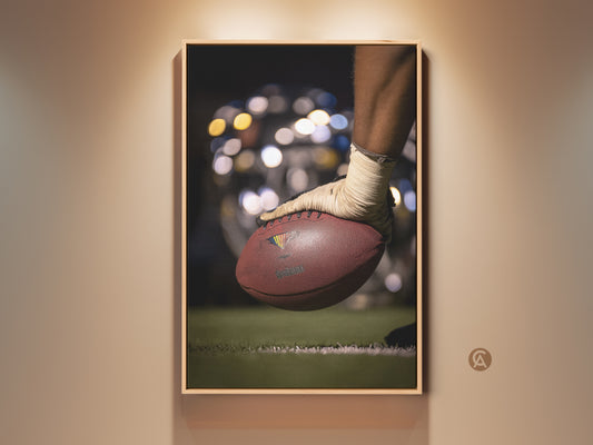 This sports wall artwork features a close-up of a football. A player's hand is shown ready for action. The brown and green tones give it a contemporary feel. Perfect man cave decor. This canvas print captures the essence of the game. Ideal gift for sports fans seeking athletic energy in their space.