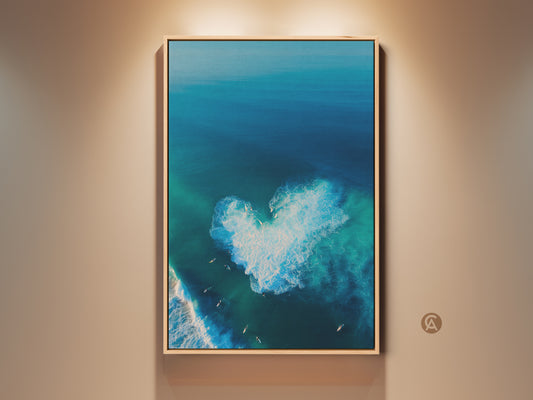 Framed beach art captures the ocean's beauty. This aerial view reveals a heart-shaped wave. Surfers dot the scene. The wall art has a natural wood frame. It enhances coastal decor. The artwork brings a serene ocean vibe to any space.