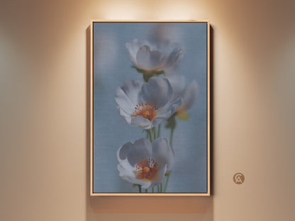 Soft Focus Floral Art Print in a wooden frame. This delicate white flower canvas art adds a serene touch to any room. The light blue botanical home decor suits Scandinavian or minimalist styles. It's a thoughtful new home gift choice. The white and orange flowers create a calming and elegant wall display.