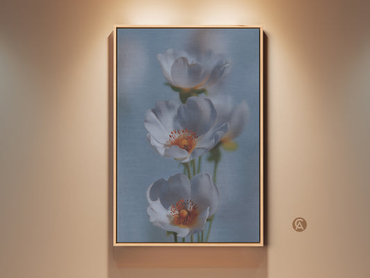 Soft Focus Floral Art Print in a wooden frame. This delicate white flower canvas art adds a serene touch to any room. The light blue botanical home decor suits Scandinavian or minimalist styles. It's a thoughtful new home gift choice. The white and orange flowers create a calming and elegant wall display.