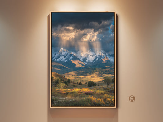 This mountain landscape canvas print captures a golden hour glow. Snowy mountains rise behind a wildflower field. Perfect farmhouse decor brings outdoor beauty indoors. A gift for outdoor lovers. The deep blue sky contrasts with golden brown earth tones.