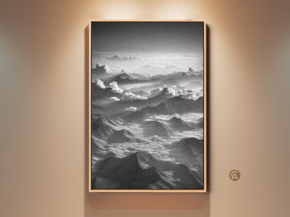 Framed monochrome mountain wall art showcases an aerial landscape canvas print. Black and white clouds artwork enhances modern nature decor. This serene mountainscape is a perfect gift for hikers. The black frame adds a sleek touch. This artwork complements any home interior wall.