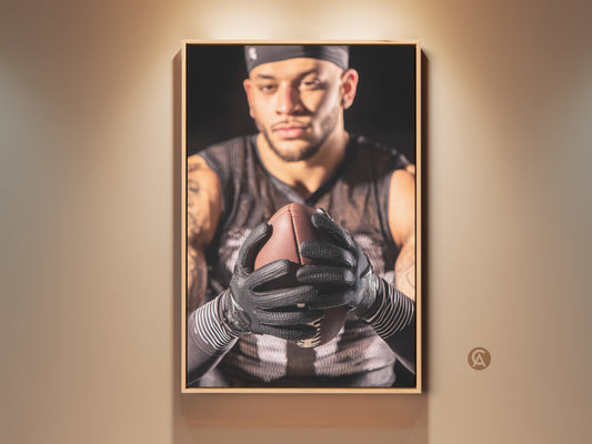 Framed American Football art print displayed on a tan wall. This athlete portrait brings intense sports decor to any room. The brown frame enhances the artwork. Ideal for a home gym or man cave. Get this sports wall decor today as a gift for a football fan.