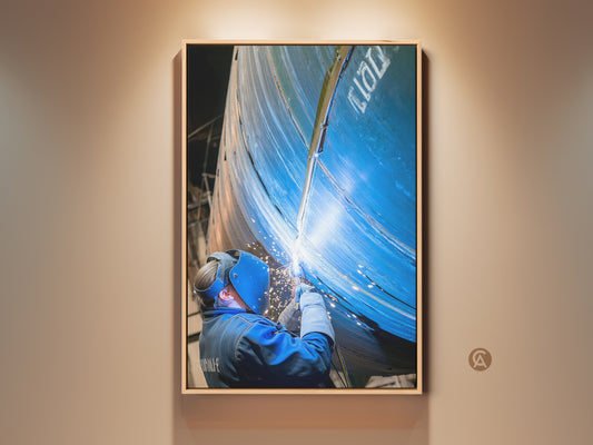 Industrial Wall Art shows a welder at work. Sparks fly in blue and orange hues. This canvas print captures craftsmanship and labor. The artwork is framed and displayed indoors adding a powerful touch to the room.