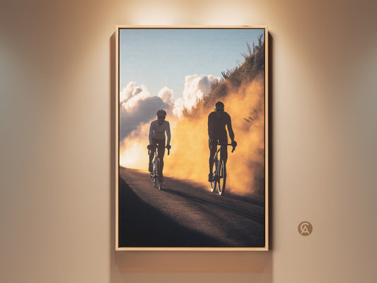 Silhouette Cyclists Wall Art print. This action photography decor features cyclists on a road during the golden hour. The sky blue and orange art style adds a contemporary touch. This piece makes a great gift for cyclists and a striking addition to any room.