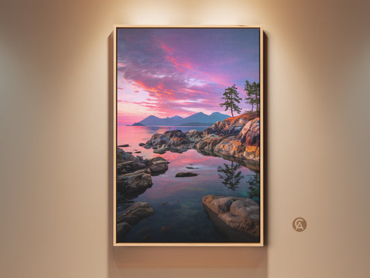 Framed rocky coastline canvas art featuring a vibrant coastal sunset. Pine trees are silhouetted against a pink and purple sky. Ocean view wall decor brings nature indoors. A perfect housewarming gift for coastal home decor.  The frame is made of light-colored wood.