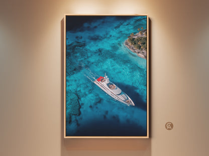 Framed aerial artwork showcasing a yacht sailing on turquoise waters near a tropical island. The art is displayed in a warm-toned frame creating a luxurious nautical theme. This eye-catching wall art brings a serene coastal vibe to any space. Perfect for yachting enthusiasts and lovers of ocean scenery.