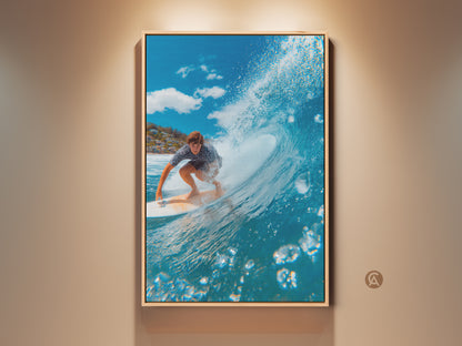 Surfer artwork on canvas. A man rides a wave in a wooden floating frame. The ocean wave curls above him. Bubbles rise in the foreground. A coastal community is visible in the background. This surfing wall art brings the ocean to any room.